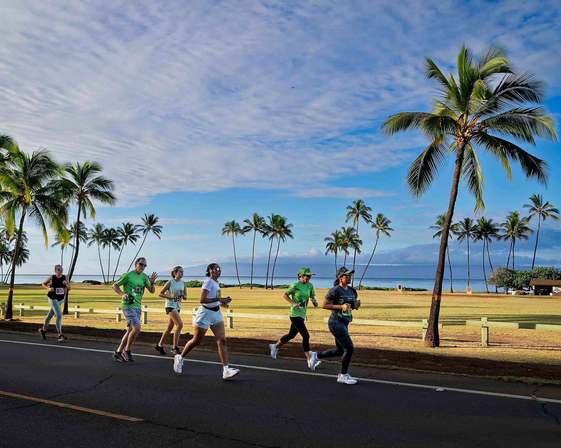 Runners pass coconut palms along the coastal road in Kaunakakai