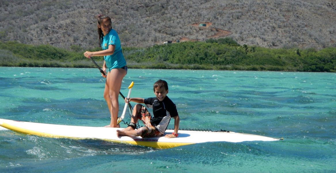 Two keiki share a paddleboard in turquoise water