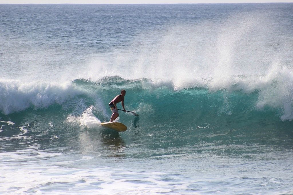 A paddler rides a breaking turquoise wave